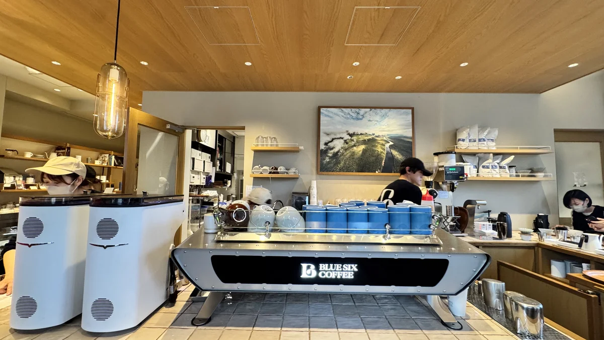 BLUE SIX COFFEEのエスプレッソマシンとバリスタ。背後にコーヒー農園の絵画