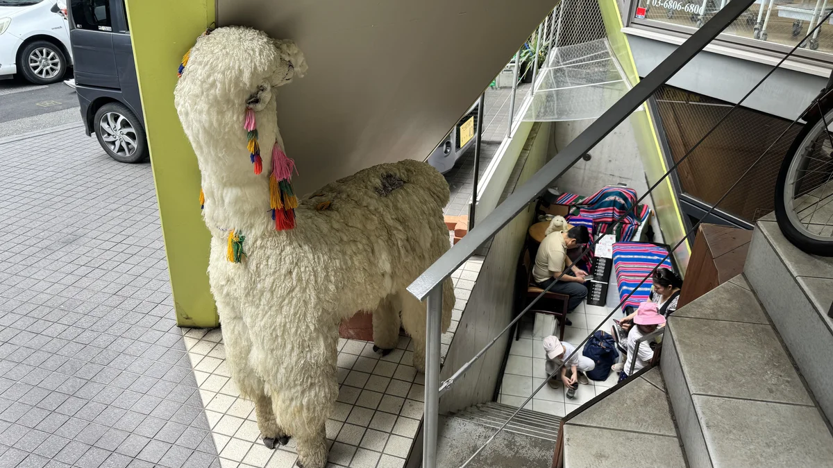 ペルー料理ALDO南青山店の入口に置かれた等身大アルパカのぬいぐるみと、階段下で過ごす来店客たち