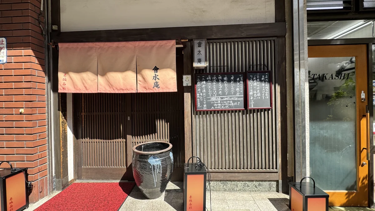 會水庵の外観。茶色いのれんに「會水庵」の文字、黒い甕と提灯、赤い絨毯の入口