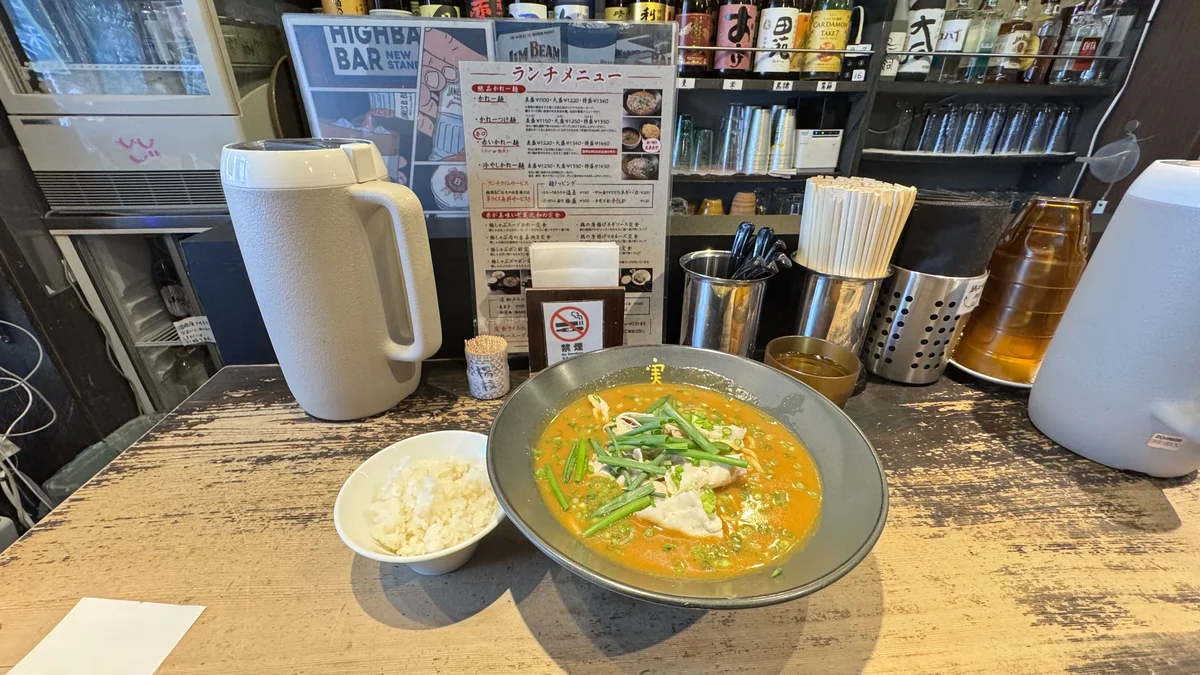 麺酒房 実之和のかれー麺をカウンターで撮影。奥にランチメニュー表とお酒の瓶が並ぶ