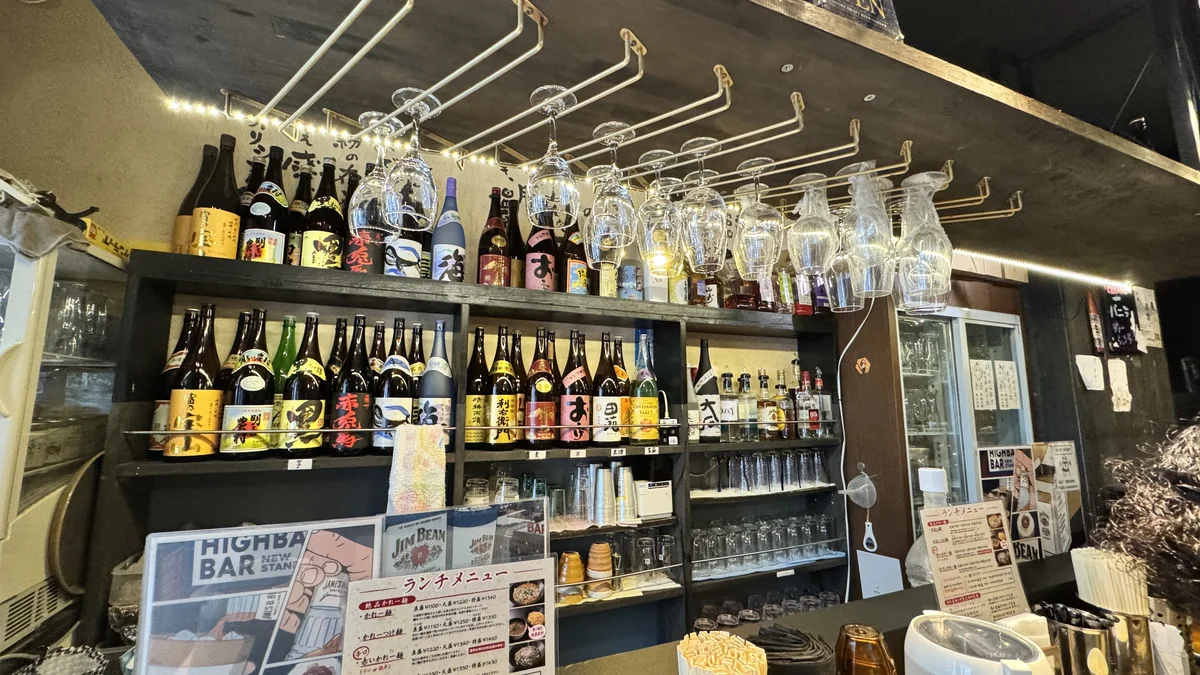 麺酒房 実之和の店内。天井から吊るされたワイングラスと、ずらりと並ぶ日本酒・焼酎のボトル