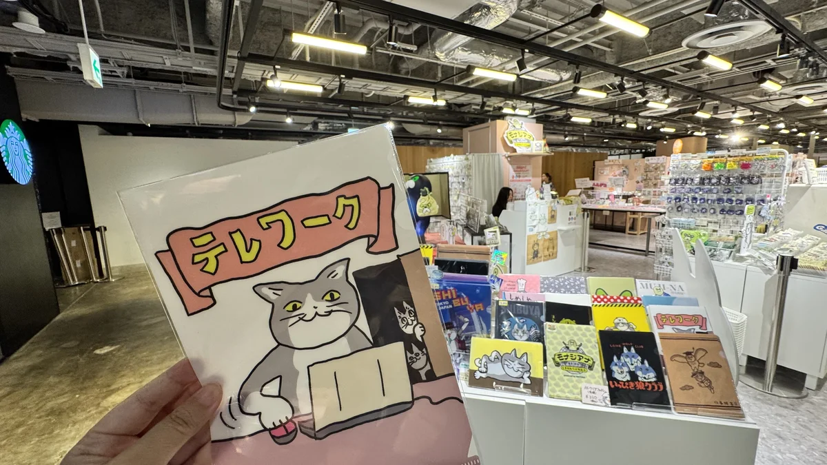 モナジアナで購入した仕事猫「テレワーク」クリアファイルを手に持ち、店内の商品棚を背景に撮影