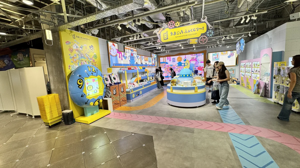 たまごっち ふぁくとり～！TAMAGOTCHI FACTORY入口の黄色い看板と大きな時計型たまごっちオブジェ、ガシャポン列