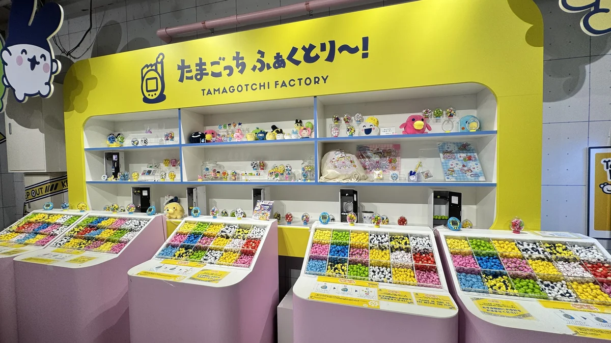 たまごっち ふぁくとり～！棚に並ぶキャラクターグッズと、カラフルな豆型ミニフィギュアが詰まったガシャポン投入口