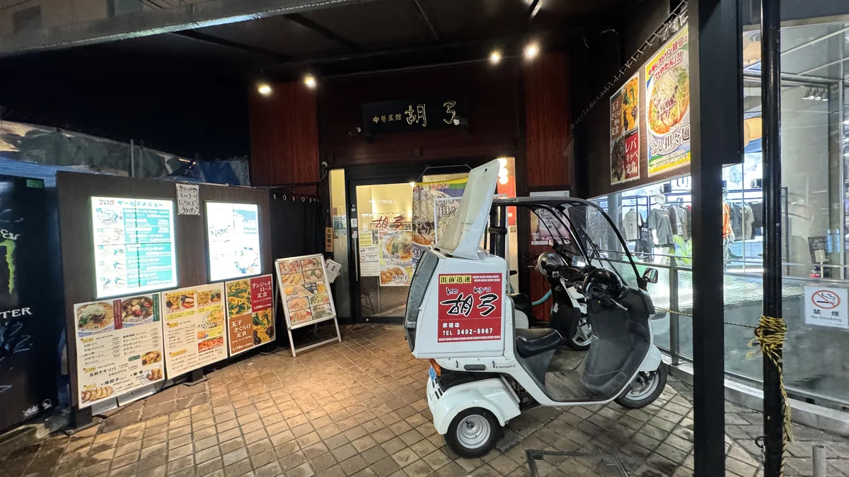 中華菜館胡弓原宿店の入口。出前用スクーターとメニュー看板が並ぶ店頭
