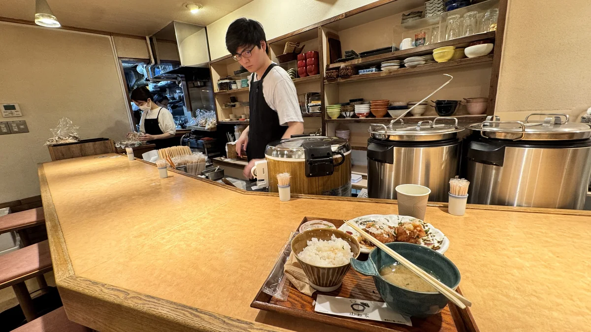 山ね家のカウンター内、食器が並ぶ棚とスタッフの様子