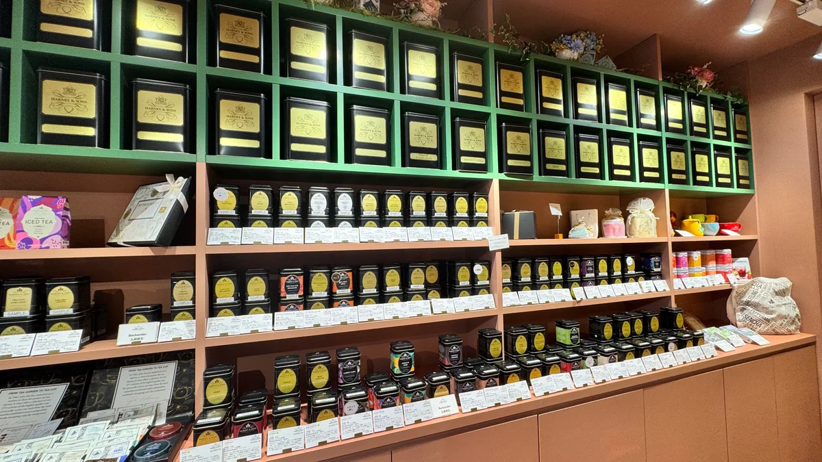 Wall shelves at the HARNEY & SONS Omotesando store. The top green shelf is lined with rows of black cans featuring the Gold Label.