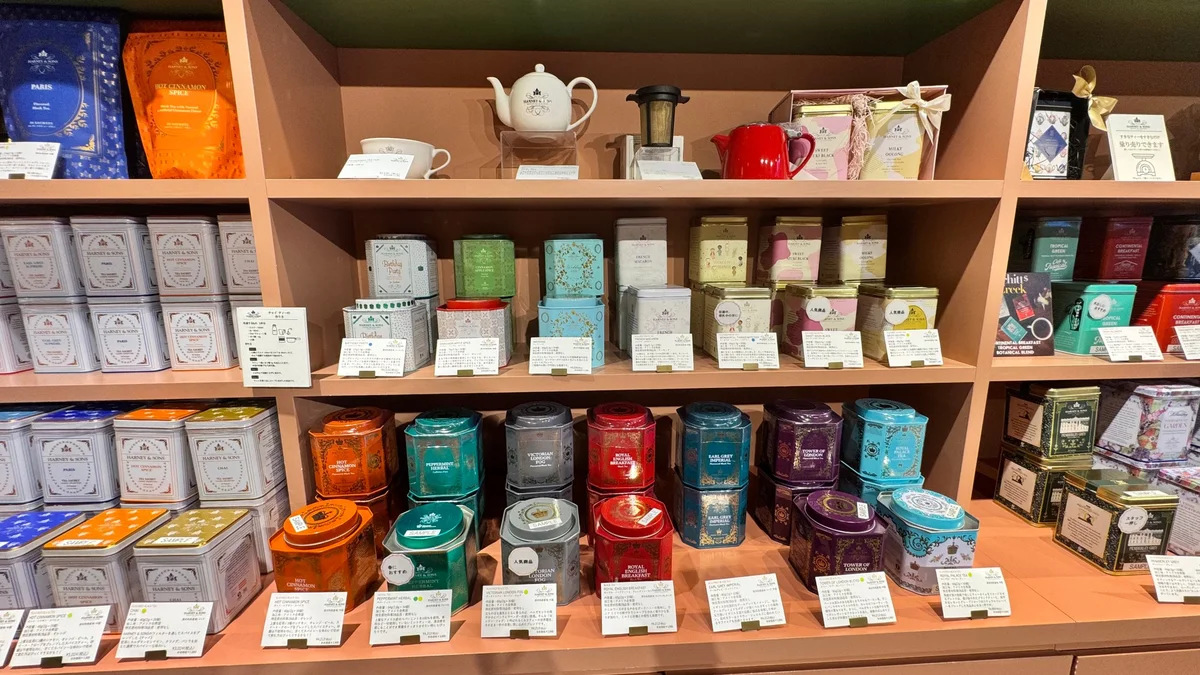 A shelf lined with HARNEY & SONS teapots, tea strainers, and hexagonal tins. Items such as “Victorian London Fog,” which features a sticker indicating it’s a popular product, and others.
